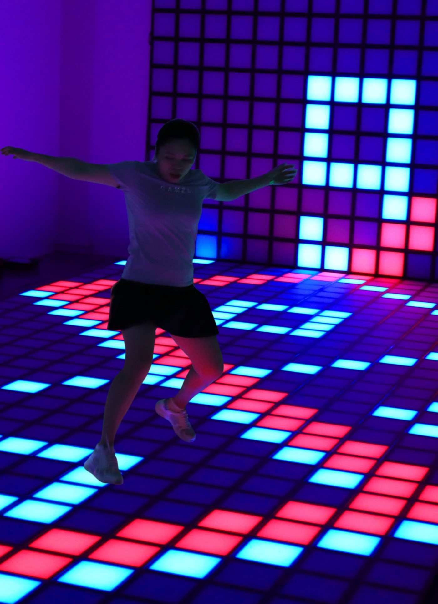 Player mid-jump on an interactive LED floor with a lit wall behind
